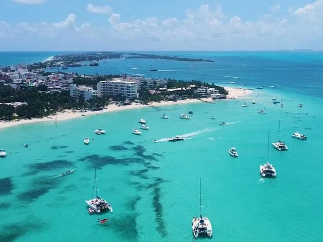 Veduta aerea di un'isola tropicale con acqua azzurra e cristallina, barche e resort.
