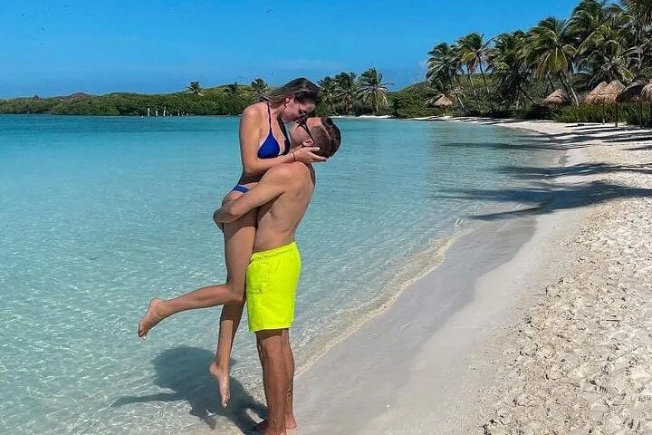 Una coppia che si abbraccia su una spiaggia tropicale di sabbia bianca con acqua azzurra e cristallina.