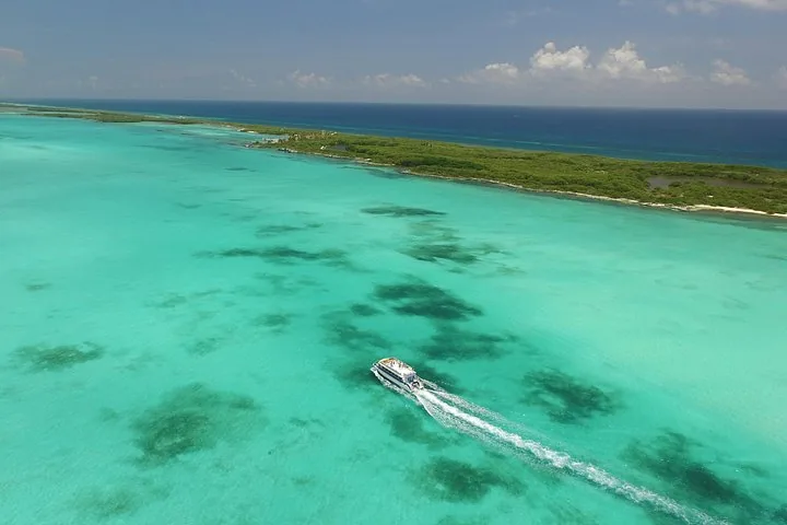 Boot fährt durch klares türkisblaues Wasser nahe der Küste von Isla Contoy.